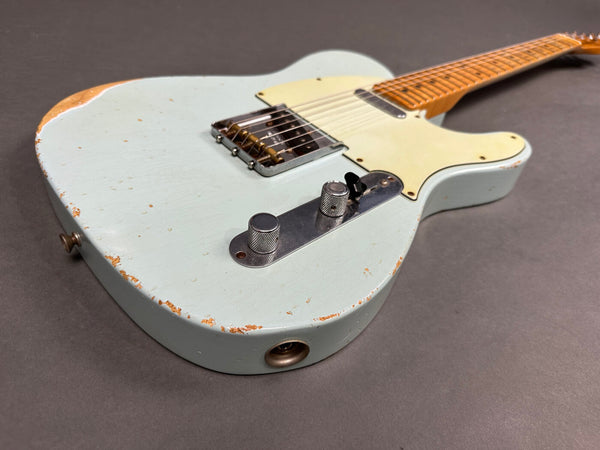 Light blue vintage electric guitar with cream pickguard and maple neck showing wear and relic paint chipping on gray background