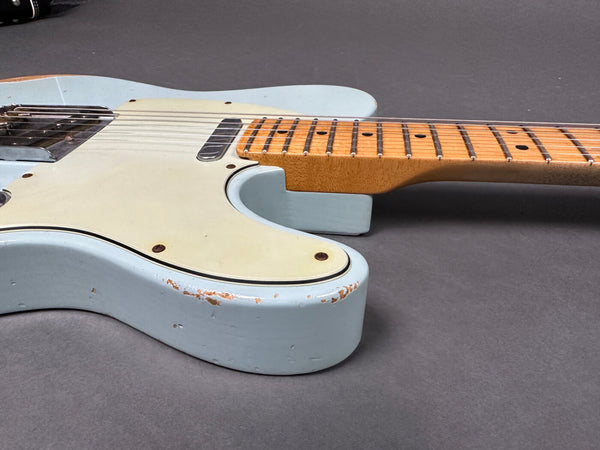 Close-up of light blue electric guitar body with visible wear and aging, showcasing cream pickguard and maple neck on gray background