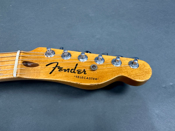 Close-up of Fender Telecaster guitar headstock with tuning pegs and strings on gray background