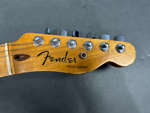 Close-up of the headstock of a Fender Telecaster electric guitar showing tuning pegs and strings on a wooden finish background