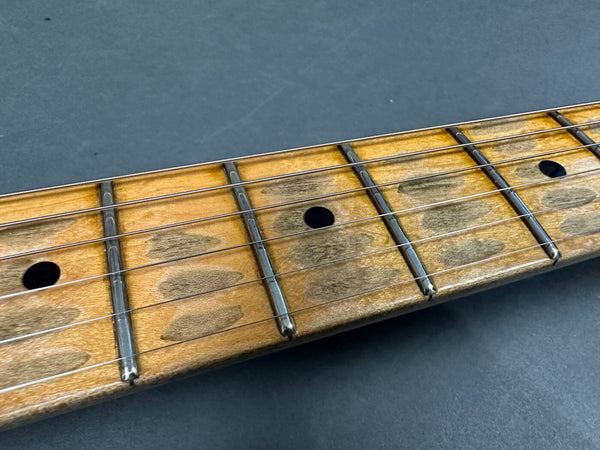 Close-up of guitar fretboard showing worn maple wood and metal frets with black dot inlays on dark background