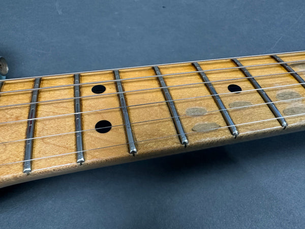 Close-up of worn maple guitar fretboard with metal frets and black dot inlays on dark background