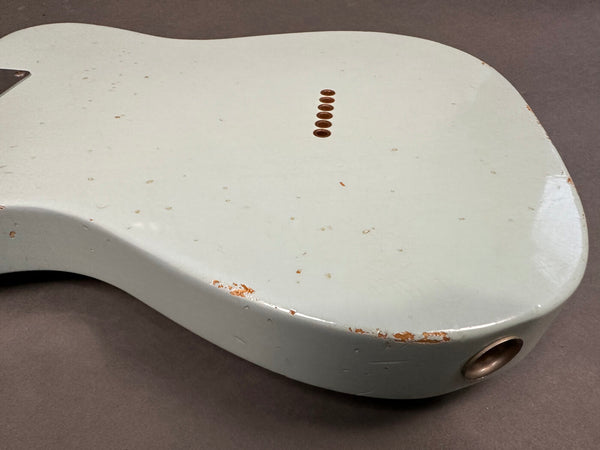 Close-up of back of vintage white electric guitar body with aged finish and worn edges, showing string ferrules and output jack socket, on gray background.