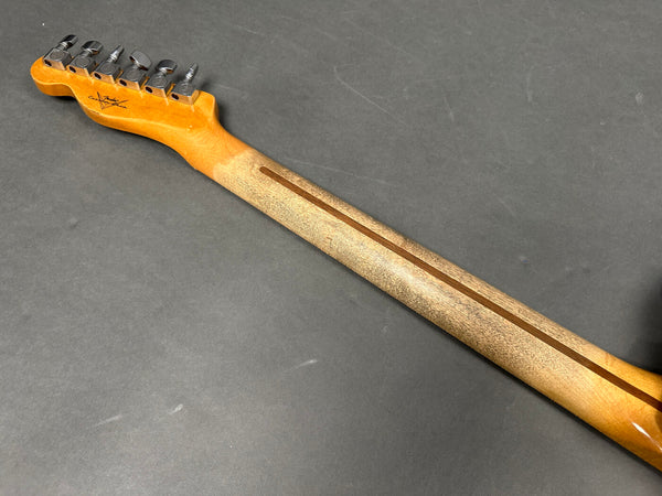 Back of maple electric guitar neck with inline tuning pegs on gray surface, vintage-style guitar tuners, Fender Custom Shop logo on headstock