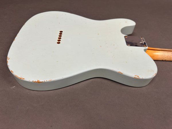 Back of vintage white electric guitar body with wear and paint chipping, bolt-on maple neck visible, on gray background.