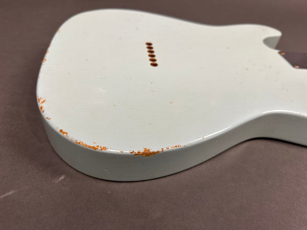 Close-up of vintage white electric guitar body showing worn paint and chipped edges with visible wood underneath on a brown background