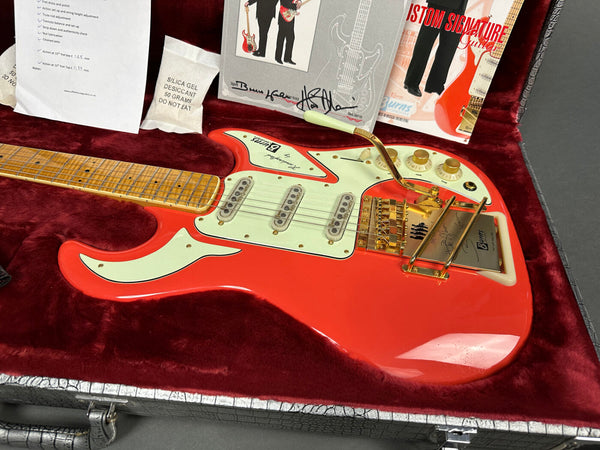 Red electric guitar with white pickguard and gold hardware in red velvet-lined hard case with paperwork and silica gel packet
