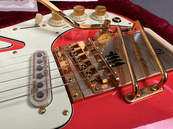 Close-up of red electric guitar bridge and gold tremolo system with white pickguard and gold control knobs showing volume and tone settings