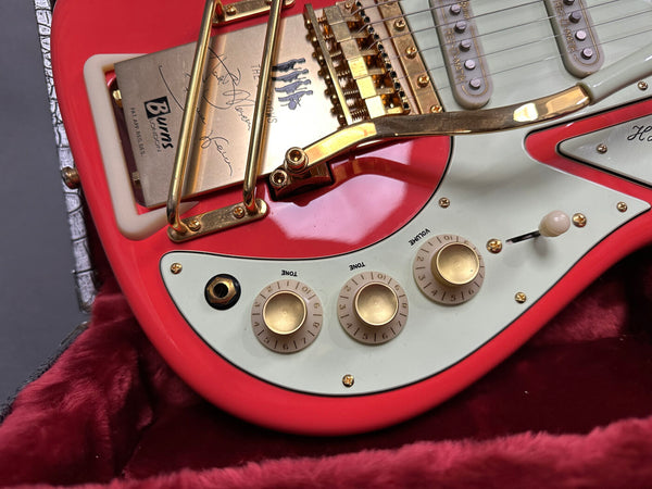 Close-up of red electric guitar control knobs, white pickguard, and gold bridge with tremolo arm in red velvet case