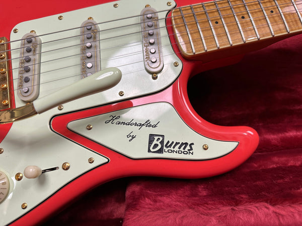 Close-up of red Burns London electric guitar body with white pickguard, vintage pickups, and "Handcrafted by Burns London" logo on pickguard.