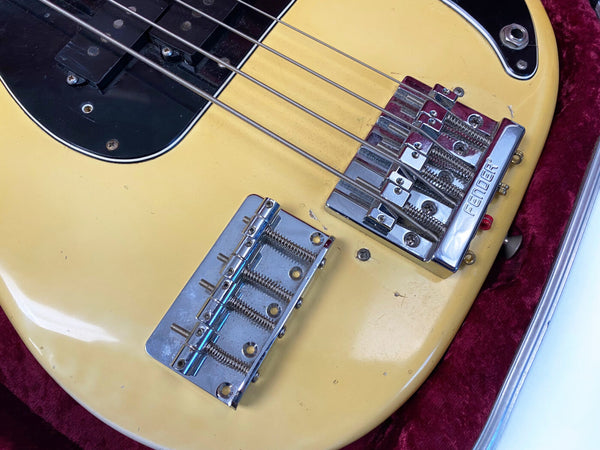 Close-up of vintage Fender bass guitar bridge and pickup on a yellow body with black pickguard in red velvet case