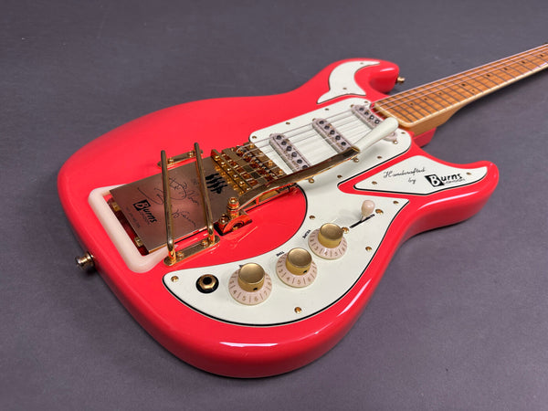Red Burns London electric guitar with white pickguard, three single-coil pickups, gold hardware, and vintage-style tremolo on gray background
