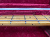 Close-up of maple guitar neck fretboard with metal frets and dot inlays on red velvet guitar case lining background