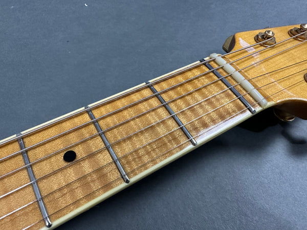 Close-up of maple guitar neck and fretboard with metal frets and steel strings on dark background