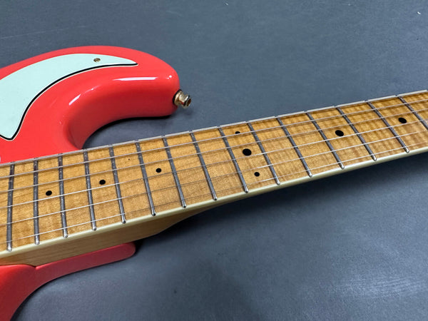 Close-up of electric guitar neck and fretboard with maple wood and dot inlays, featuring a coral red guitar body with white pickguard on a gray background