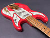 Close-up of red Burns London electric guitar with white pickguard, gold hardware, and maple fretboard on gray background