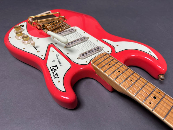 Close-up of red Burns London electric guitar with white pickguard, gold hardware, and maple fretboard on gray background