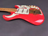 Vintage red electric guitar with white pickguards, three single-coil pickups, maple neck, and gold hardware including tremolo bridge and control knobs on dark background