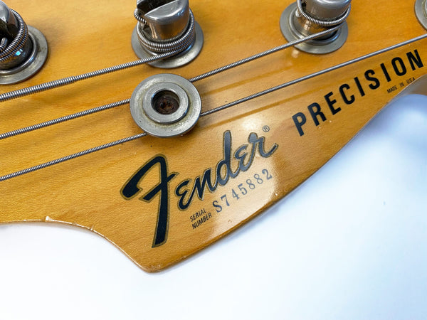 Close-up of Fender Precision bass guitar headstock with serial number S745882 and tuning pegs, vintage natural wood finish, made in USA