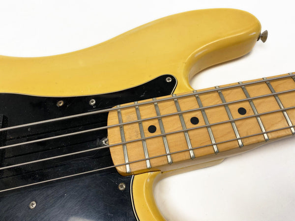 Close-up of vintage yellow electric bass guitar fretboard and strings with black pickguard against white background
