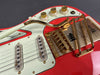 Close-up of red electric guitar body featuring gold hardware, two single-coil pickups, white pickguard, volume and tone control knobs, and a Bigsby vibrato tailpiece with gold-plated components.