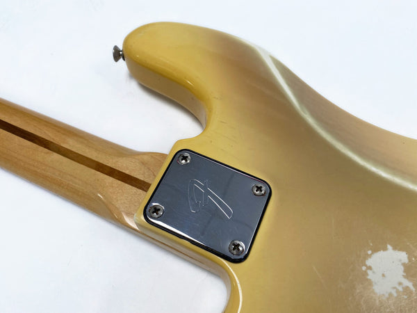 Vintage yellow electric guitar body with maple neck and a metal neck plate featuring an engraved logo, showing worn finish and scratches