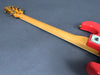 Rear view of electric guitar neck with maple wood finish and red body on gray background showing tuning pegs and neck joint plate