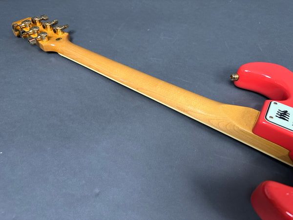 Rear view of electric guitar neck with maple wood finish and red body on gray background showing tuning pegs and neck joint plate