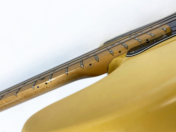 Close-up of the neck and fretboard of a yellow electric bass guitar showing metal frets, dot inlays, and strings against a white background.