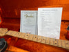 Close-up of Fender 1956 Stratocaster NOS guitar neck with Certificate of Authenticity and Coffee House Guitars pre-sales checklist in orange plush guitar case