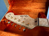 Close-up of Fender Stratocaster electric guitar headstock with gold tuning pegs and birdseye maple finish resting inside orange plush guitar case interior