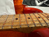 Close-up of electric guitar maple fretboard with stainless steel frets and round black dot inlays on red guitar body against orange textured background