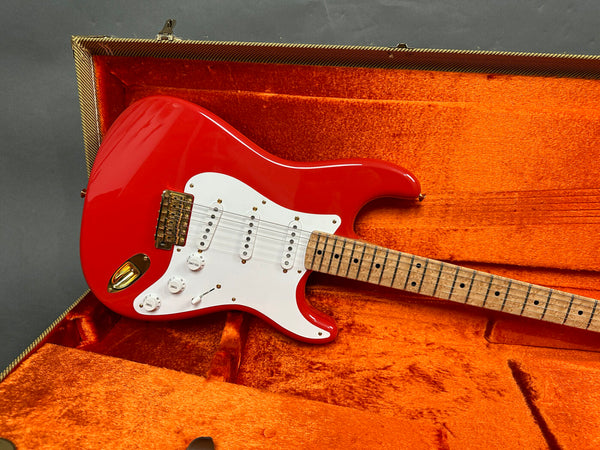 Red electric guitar with white pickguard and maple neck in orange plush-lined guitar case