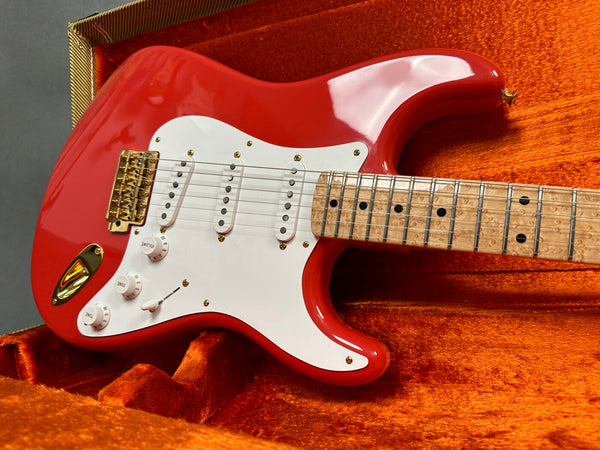 Red electric guitar with white pickguard and three single-coil pickups, maple birdseye fretboard, and gold hardware in orange plush guitar case