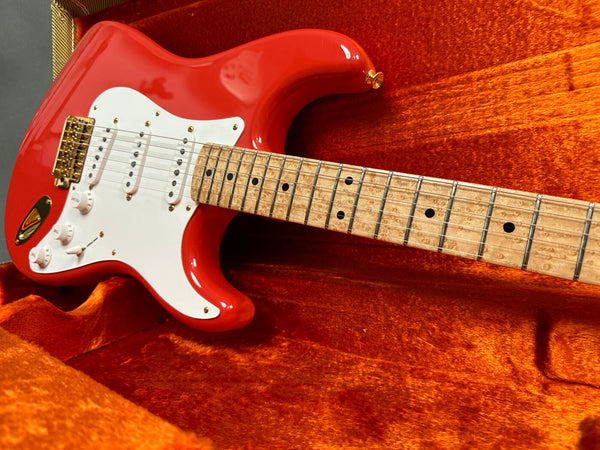 Red electric guitar with white pickguard and birdseye maple fretboard inside orange velvet guitar case