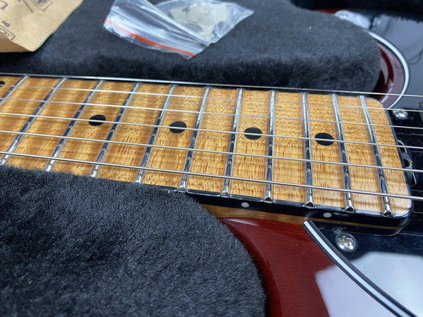 Close-up of electric guitar maple fretboard with dot inlays and steel strings on cherry red body, displayed on black plush surface