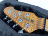 Close-up of natural wood grain Music Man Stingray electric guitar headstock with chrome tuning pegs inside black plush guitar case