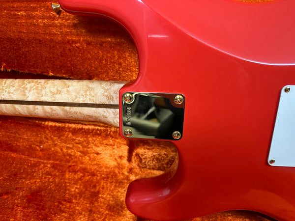 Close-up of red electric guitar heel plate with serial number on maple neck and orange plush guitar case interior background