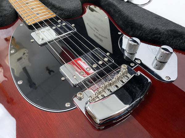 Close-up of red electric guitar body with chrome bridge, pickups, and control knobs, wooden neck, and black pickguard in guitar case interior.