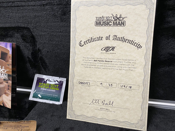 Ernie Ball Music Man Certificate of Authenticity for Ball Family Reserve limited release guitar, serial number 686097, handwritten signature of Scott Ball, Vice President, with Ernie Ball string cleaner packet on black fabric background.