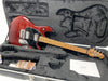 Ernie Ball Music Man StingRay electric guitar in transparent red finish with maple neck and black pickguard, displayed in a black plush-lined guitar case with accessories and paperwork.