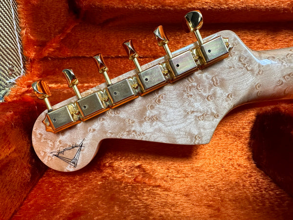 Close-up of guitar headstock with gold tuning pegs and unique birdseye maple wood grain, resting on orange plush case interior