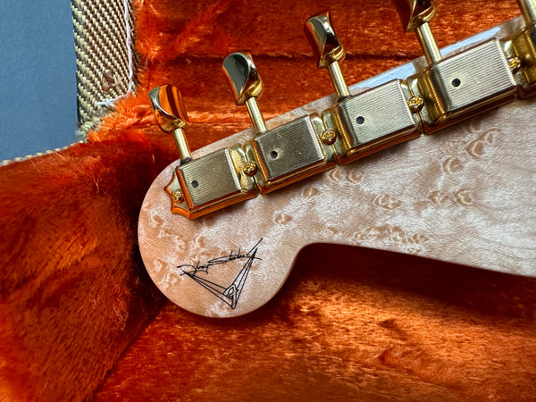 Close-up of guitar headstock with gold tuning pegs and signature detail inside orange plush guitar case