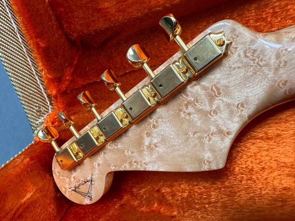 Close-up of guitar headstock with gold tuning pegs and quilted maple wood grain on orange plush guitar case lining