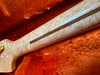 Close-up of figured maple guitar neck with walnut skunk stripe and pearl inlay on orange plush guitar case lining