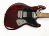 Close-up of dark red electric guitar body with black pickguard, chrome bridge cover, two chrome humbucker pickups, and maple neck with dot inlays on white background