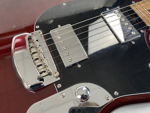 Close-up of electric guitar bridge, chrome hardware, and dual humbucker pickups on black pickguard and dark red wood body
