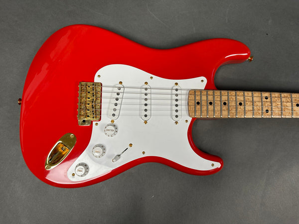 Red electric guitar with white pickguard, maple neck with birdseye maple fretboard, and gold hardware including bridge and output jack cover on gray background