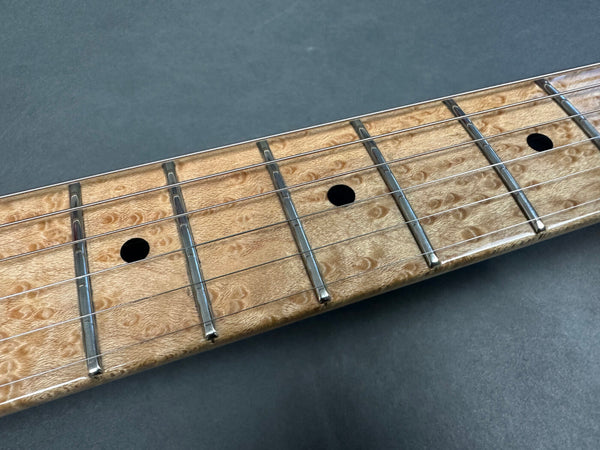 Close-up of guitar fretboard with birdseye maple wood and metal frets featuring black dot inlays and steel strings on dark gray background