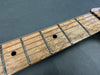 Close-up of guitar neck and frets showing birdseye maple fretboard with dot inlays and metal frets against a dark background